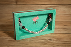 Bracelet with letter beads spelling 'THE BLACK DOG' displayed in a green glittery frame on a wooden surface.