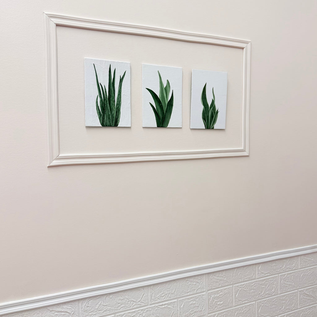Three framed pictures of green plants on a beige wall.