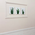 Three framed pictures of green plants on a beige wall.