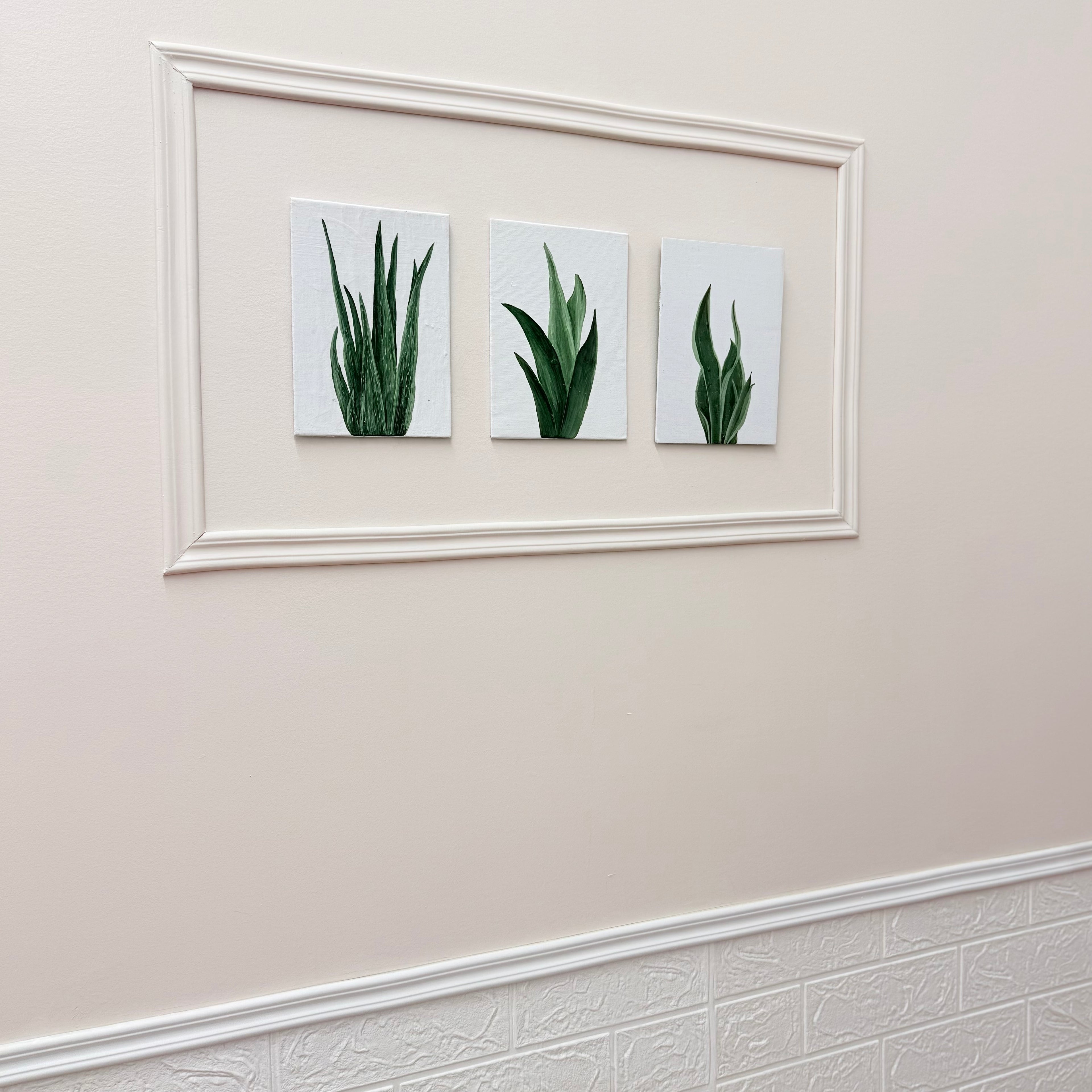 Three framed pictures of green plants on a beige wall.