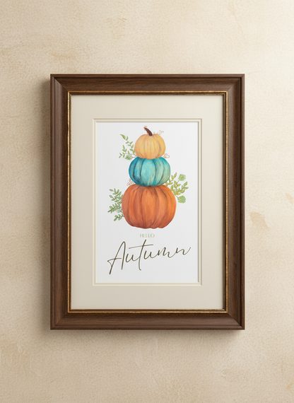Three stacked pumpkins with 'Hello Autumn' text on a white background in a brown fame on a beige wall