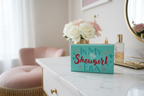Decorative box with 'In My Showgirl Era' text on a table with flowers and a mirror in the background.