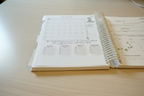 Spiral-bound planner open to an August calendar on a wooden surface