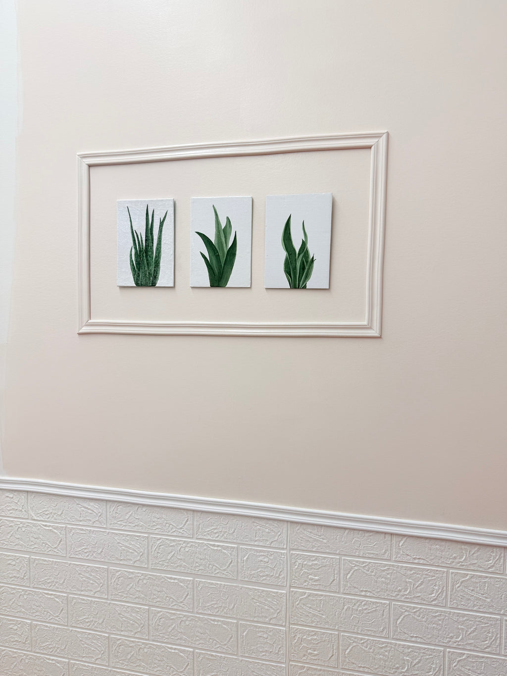 Framed artwork of three green plants on a beige wall.