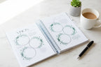 Open spiral-bound notebook with green floral designs for vision board planning. 
