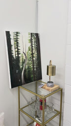 Close up video of acrylic forest painting on a gallery canvas sitting on a glass gold metal shelf with minimal decor.