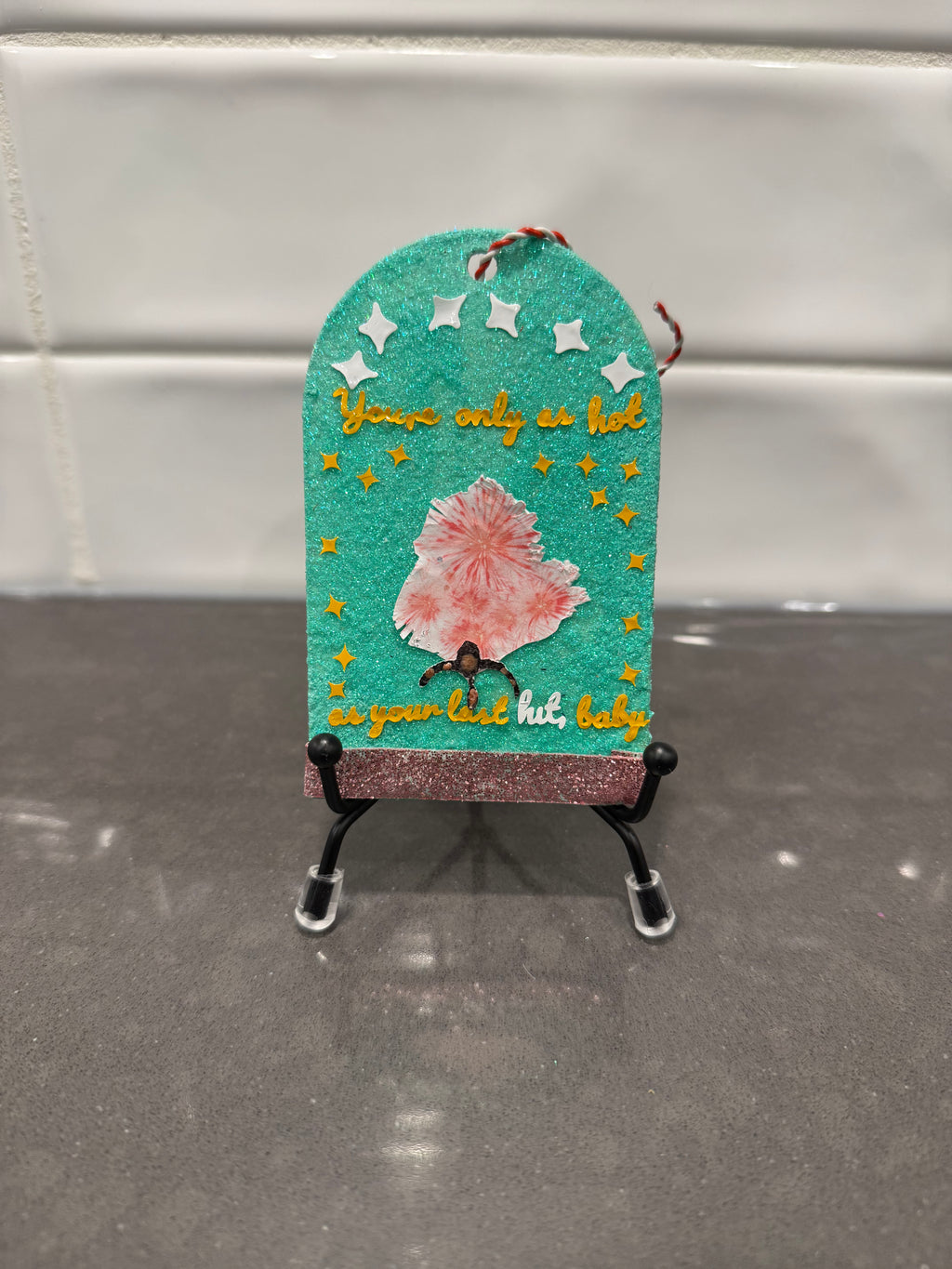 Decorative sign with text and a flower on a stand against a neutral background